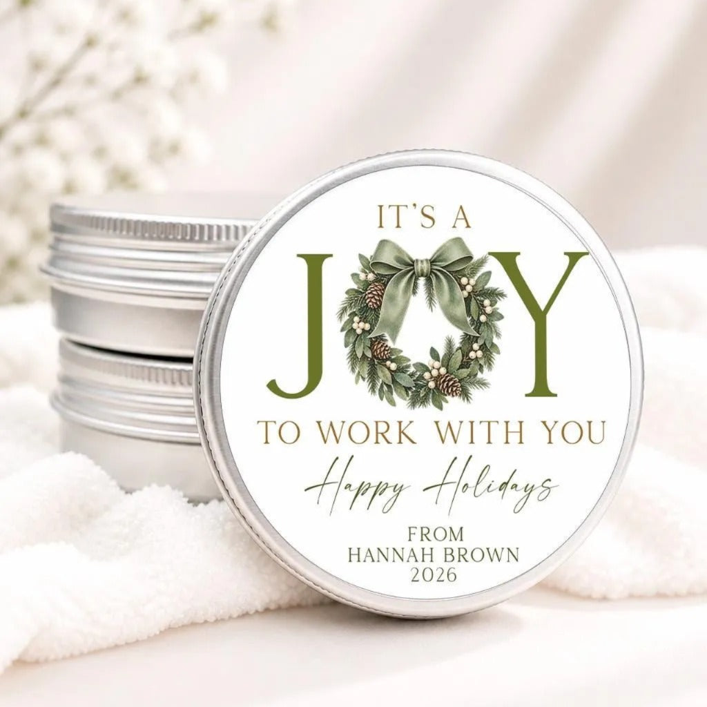 A round tin lid with a wreath design and text on it, placed on a white cloth.