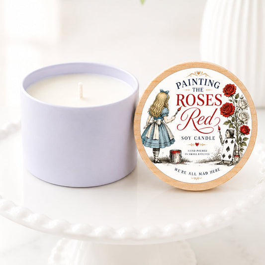 **Alt Text:**

Alice in Wonderland inspired soy candle featuring a “Painting the Roses Red” label with vintage storybook artwork of Alice painting white roses red. The candle is displayed on a white pedestal stand with a natural wood lid, surrounded by soft greenery and white florals in a bright, airy setting. Perfect for book lovers, literary gifts, Wonderland fans, and whimsical home décor.
