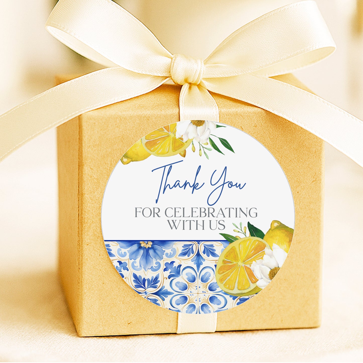 A gift box with a white ribbon and a round sticker attached to it. The sticker has a floral design and text that says "Thank You for Celebrating With Us".