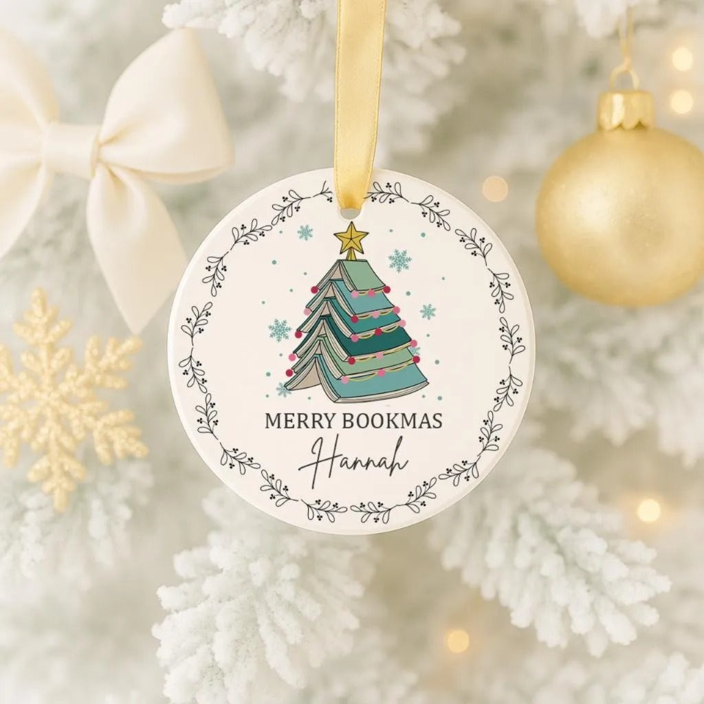 A white Christmas tree ornament with a green Christmas tree design and the text "Merry Bookmas Hannah" is hanging on the tree.