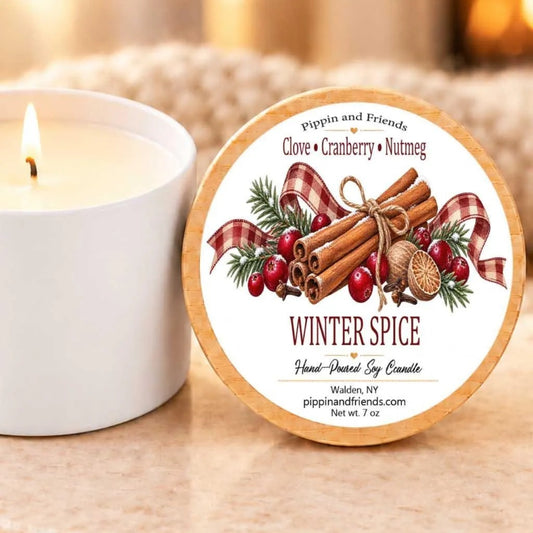 A white candle with a label that reads "Winter Spice" and "Hand-Poured Soy Candle" is placed next to a white candle holder.