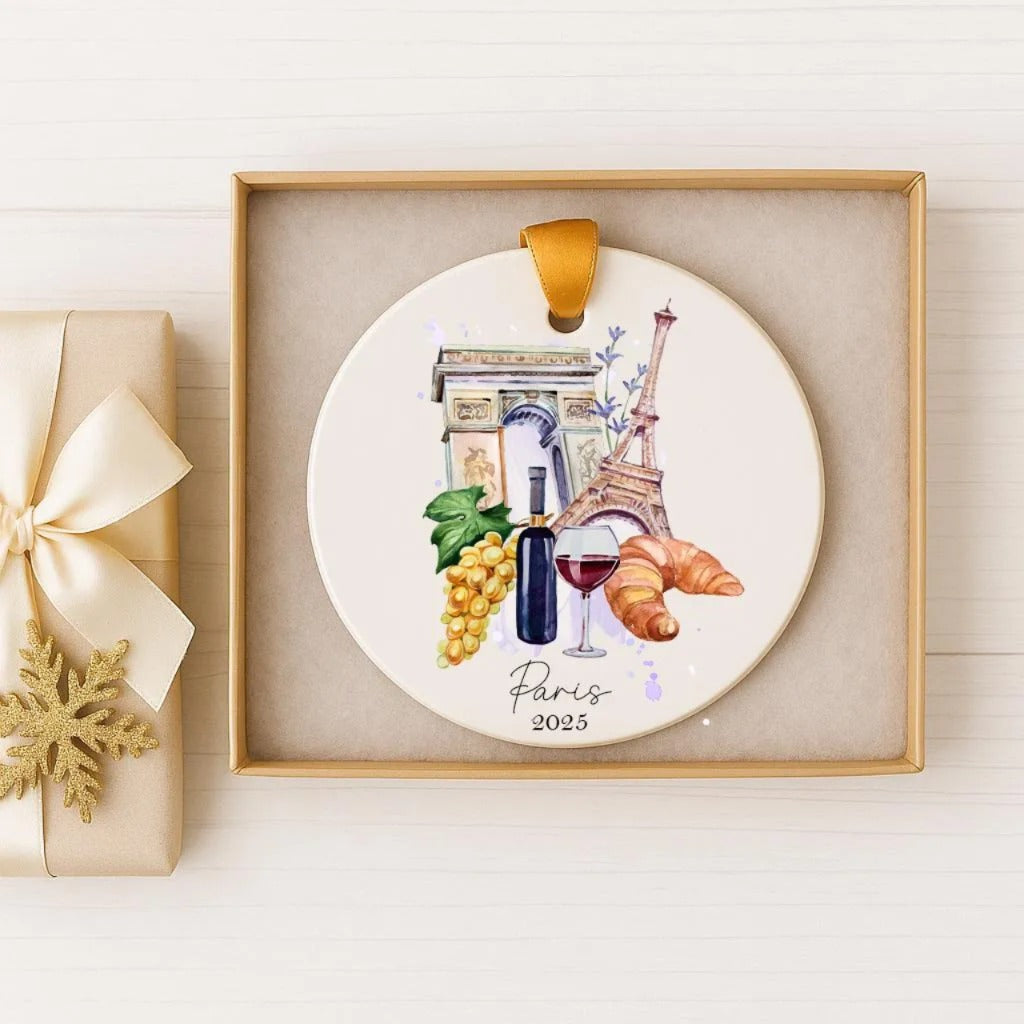 A decorative ornament featuring a Paris-themed design, including the Eiffel Tower, grapes, a wine glass, and a croissant, is displayed in a box.