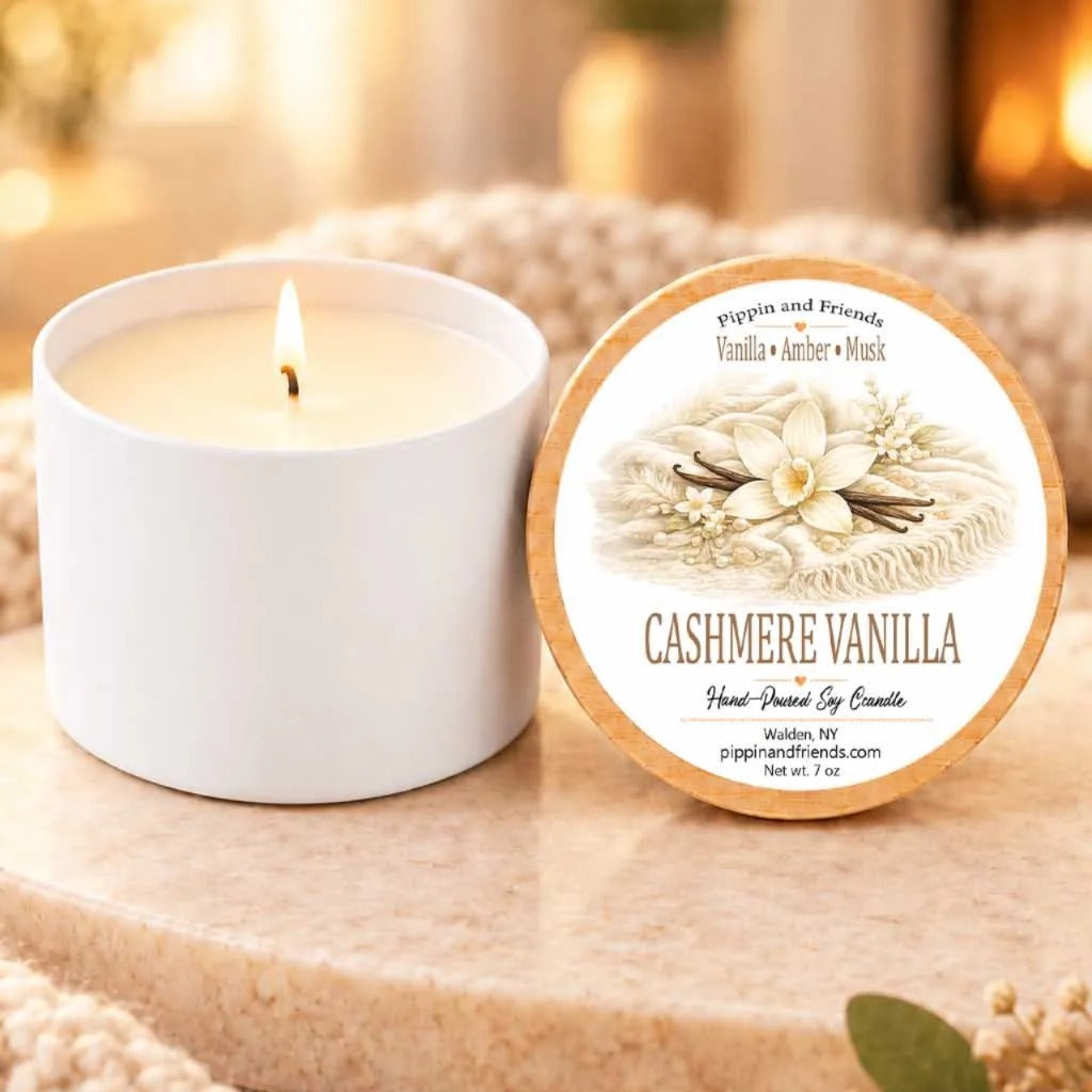 a white candle labeled "CASHMERE VANILLA" next to a white candle holder, both sitting on a wooden surface.