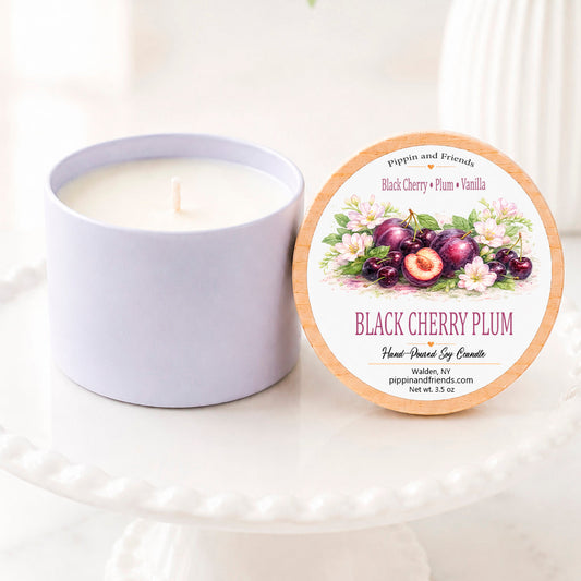 A soy candle in a white ceramic vessel with a natural wood lid featuring a watercolor black cherry and plum, hand-poured by Pippin and Friends