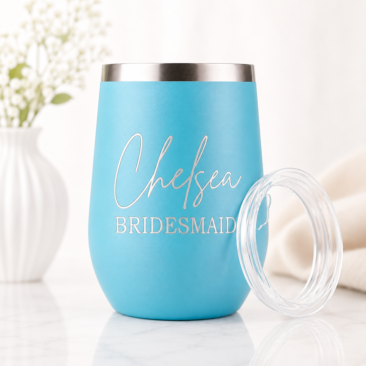 Personalized turquoise bridal party wine tumbler with custom name in elegant script and bridal party title, featuring a stainless steel rim and clear lid. Displayed on a marble surface with soft floral accents and a bright, airy background.