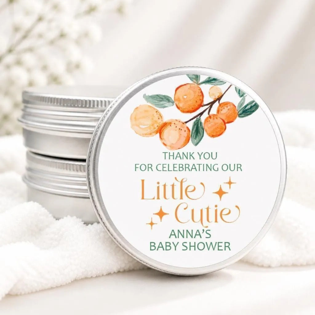 A round tin lid with a label that says "Thank you for celebrating our Little Cutie Anna's baby shower" and features an illustration of oranges on a branch.