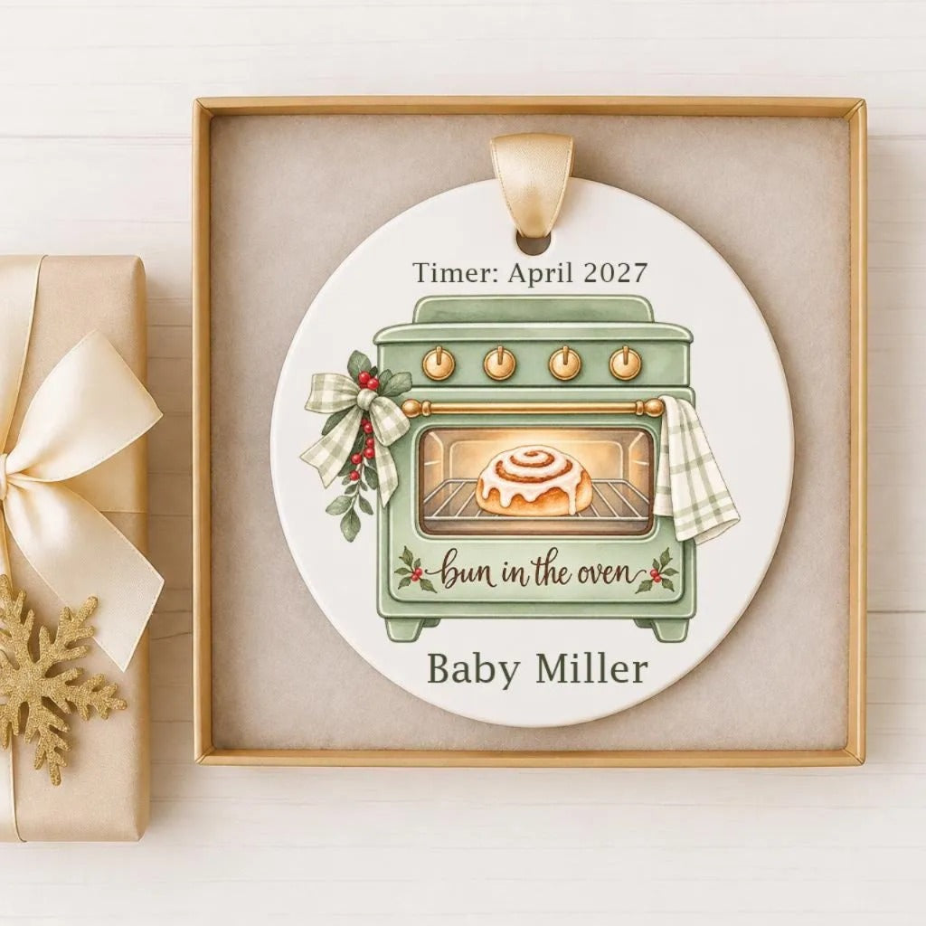 A white ceramic ornament with a green oven and a cinnamon roll inside, hanging on a wooden surface.