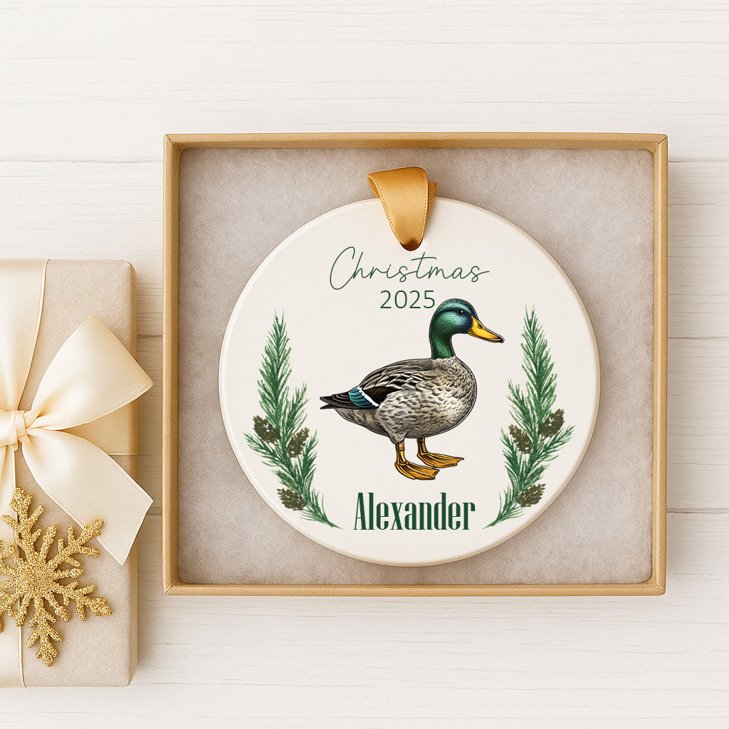 A white ceramic ornament with a duck illustration and the name "Alexander" written on it, displayed in a wooden frame.