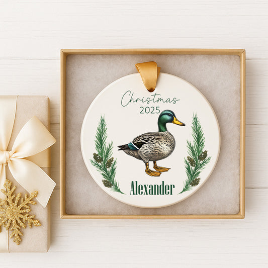 A white ceramic ornament with a duck illustration and the name "Alexander" written on it, displayed in a wooden frame.