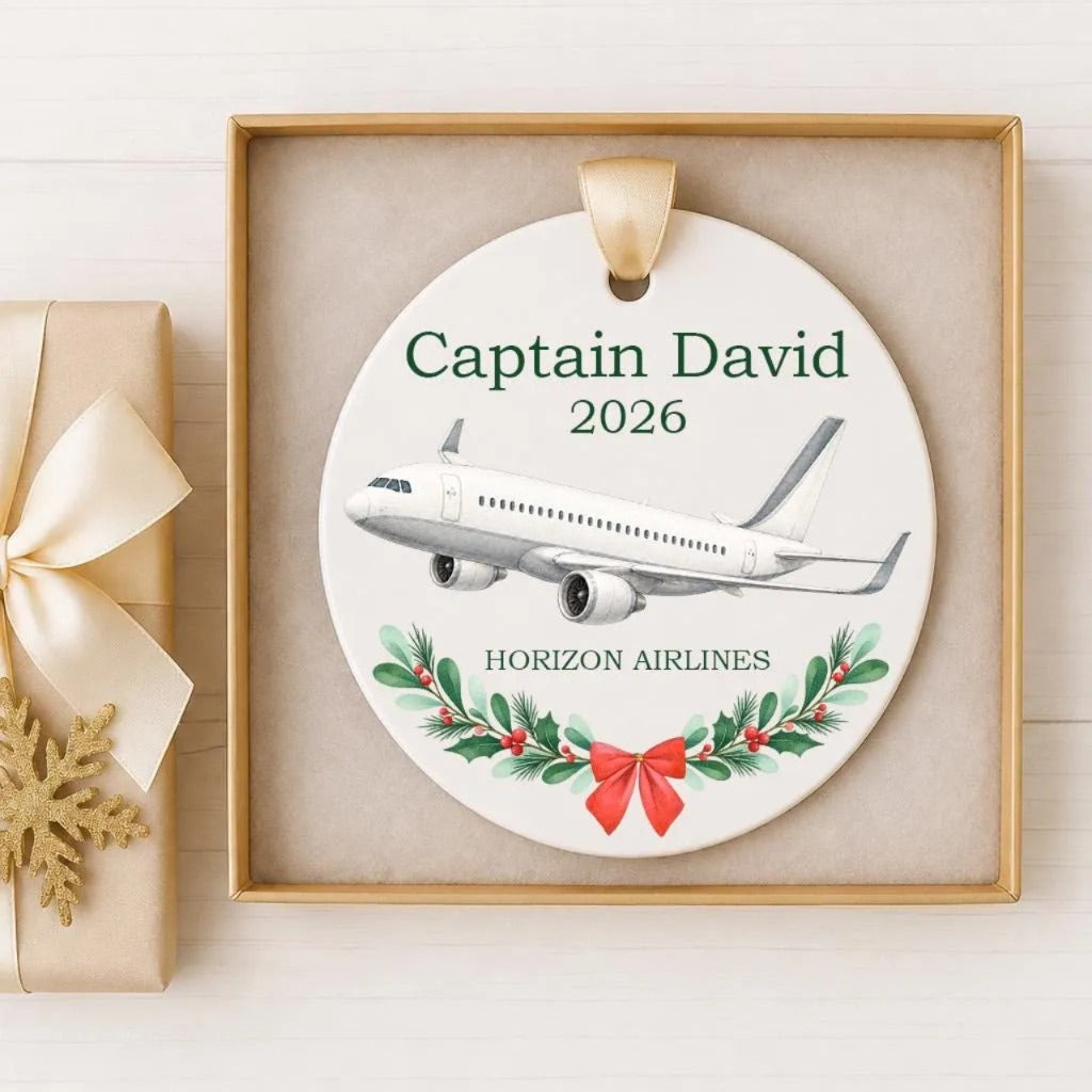 A decorative ornament with a white airplane and a wreath of greenery, placed in a gold frame.