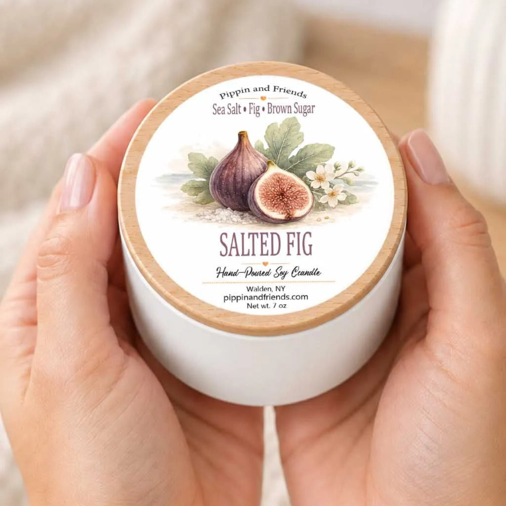 A person's hands holding a white container with a label featuring an illustration of a sliced fig and other fruits.