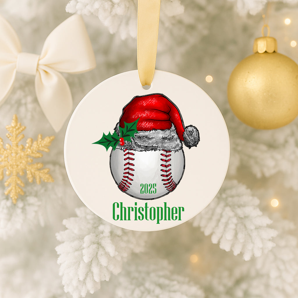 A white ornament with a baseball and Santa hat design hangs on a Christmas tree.