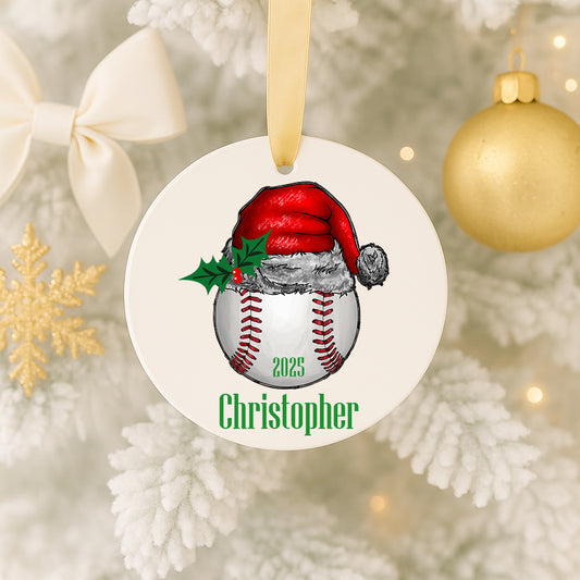 A white ornament with a baseball and Santa hat design hangs on a Christmas tree.