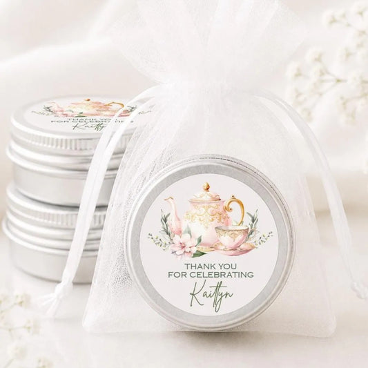 a close-up of a silver tin with a label that says "Thank you for celebrating Kaitlyn". The tin is placed on a white surface, and there are other tin containers visible in the background.
