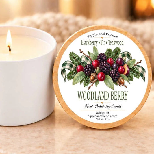 a white candle next to a wooden looking lid with a label that displays an illustration of berries and leaves.