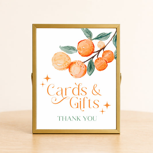 A Little Cutie baby shower cards and gifts sign with citrus design displayed on table for gift station decor.