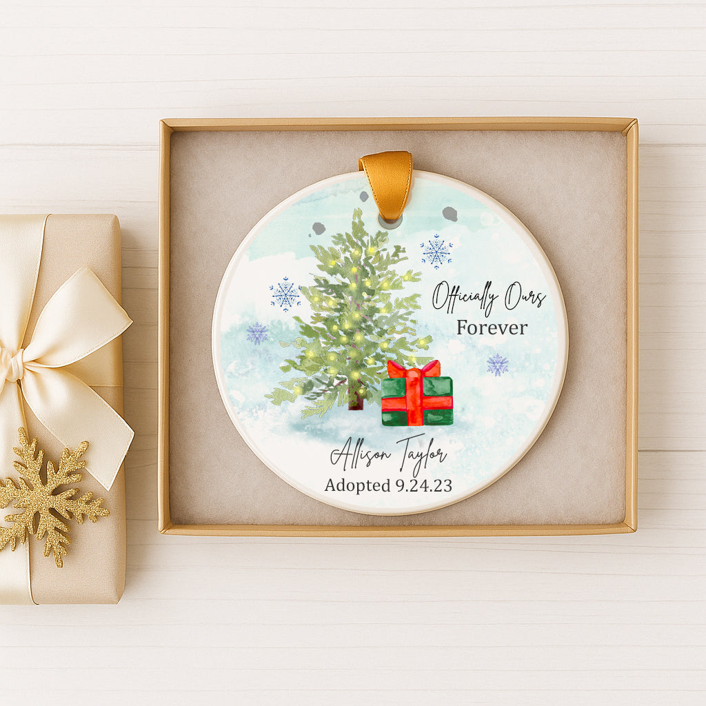 A white ceramic ornament with a Christmas tree and a red gift box, placed in a gold box.