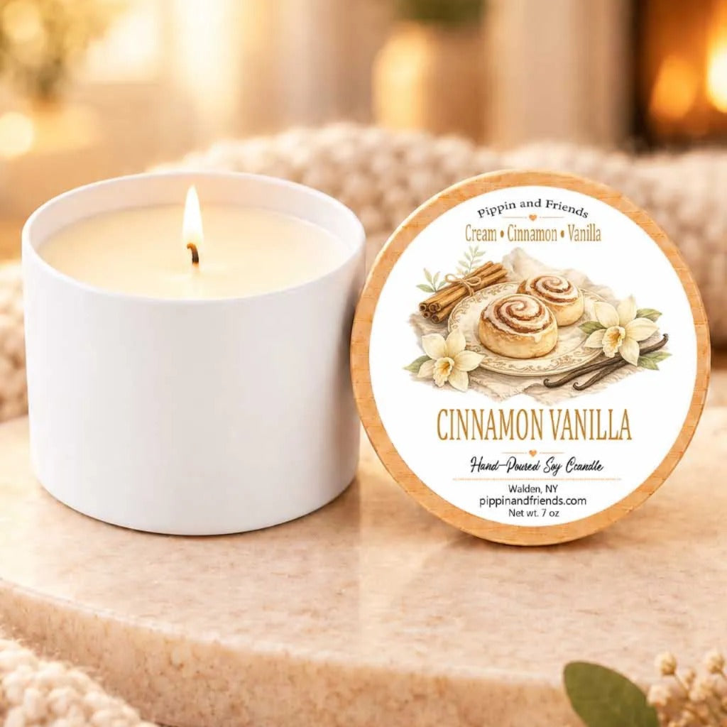 a white candle labeled "Cinnamon Vanilla" next to a white candle holder, both sitting on a wooden surface.