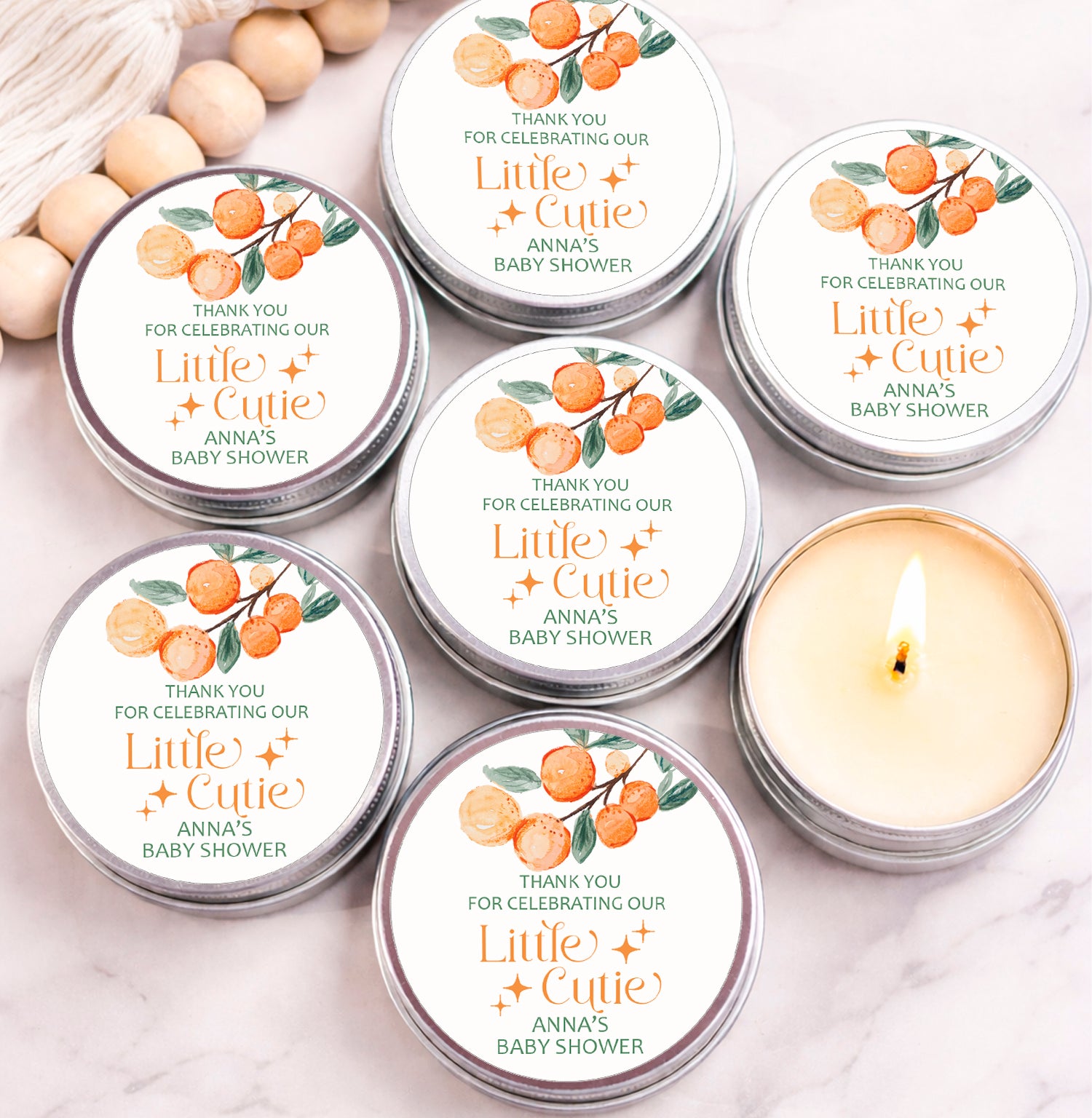 six silver tin candles with orange and green labels, arranged on a marble surface.