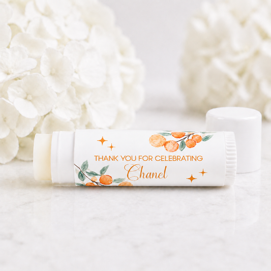 Citrus Cutie baby shower lip balm favor with personalized orange watercolor label reading thank you for celebrating Chanel on white tube with soft floral background