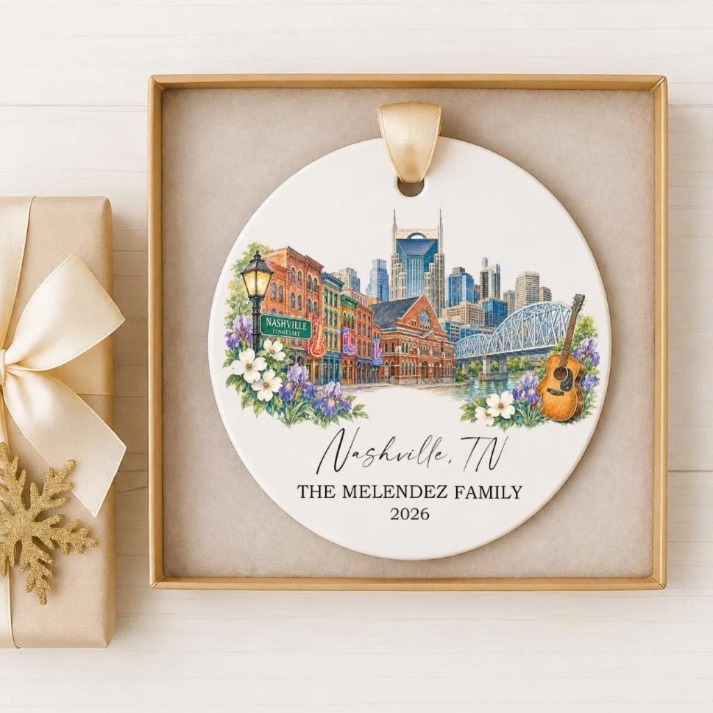 A decorative ornament featuring a cityscape of Nashville, Tennessee, with a guitar and flowers, placed in a gold frame.