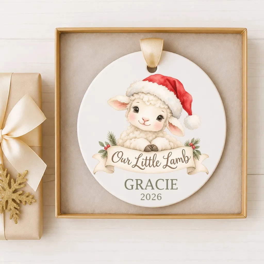 A white ornament with a lamb wearing a Santa hat and a banner that says "Our Little Lamb" and "GRACIE" is displayed in a gold frame.
