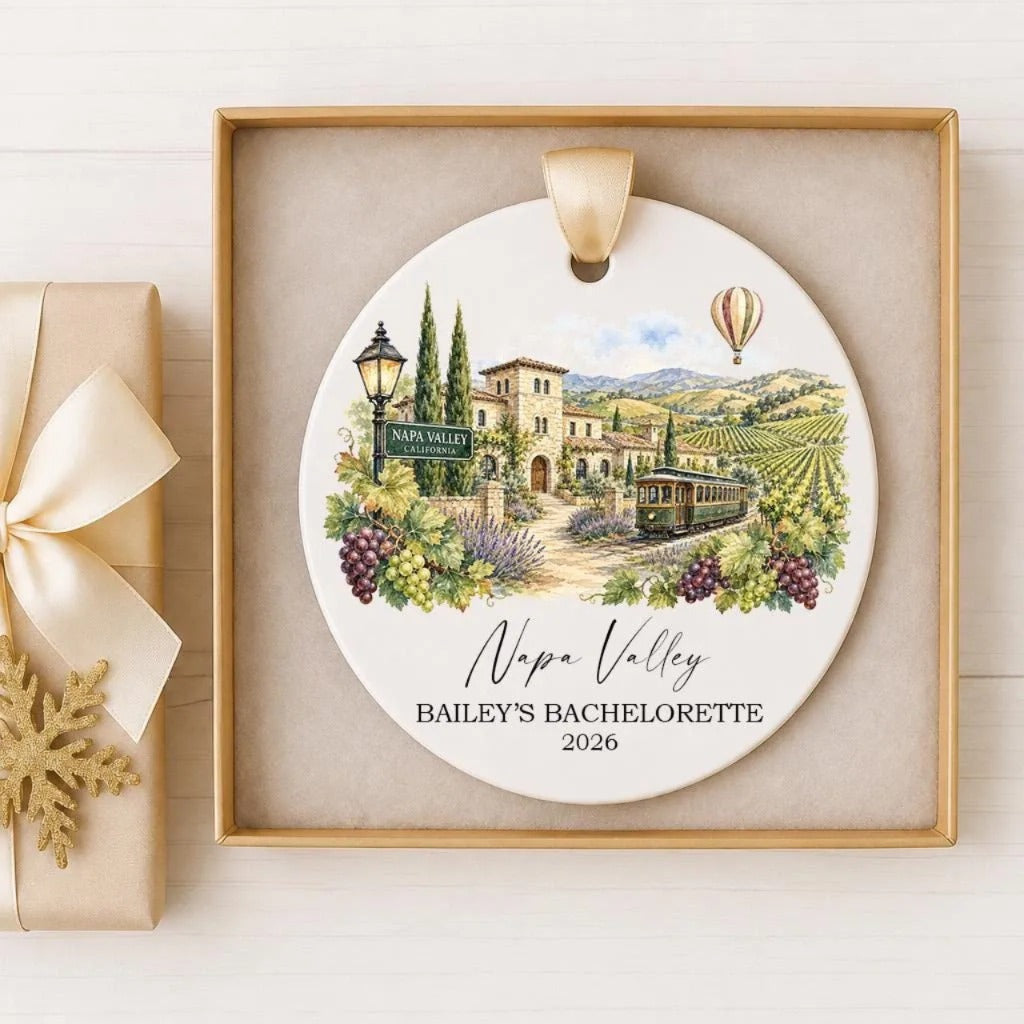 A decorative ornament featuring a scenic view of Napa Valley, with a train and hot air balloons in the background. The text "Napa Valley BAILY'S BACELORETTE 2026" is displayed on the ornament.