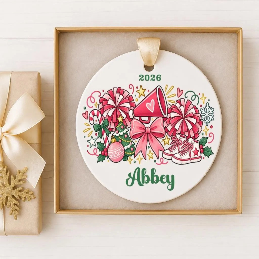A white ornament with a gold frame, featuring a Christmas tree, candy canes, and a pink bow, along with the name "Abby" written on it.
