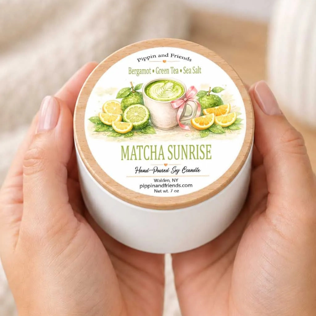 A person's hands holding a white container with a label that features an illustration of a green tea drink surrounded by citrus fruits.