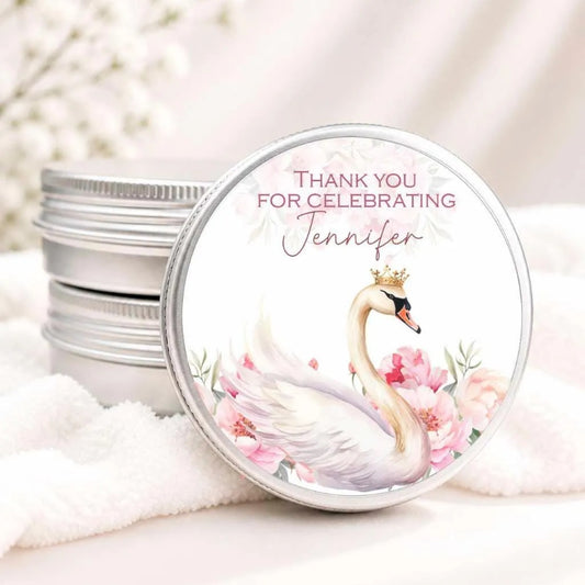 A round tin lid with a decorative image of a swan wearing a crown, surrounded by pink flowers. The lid has a message that says "Thank you for celebrating Jennifer".