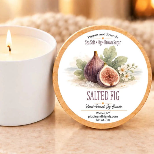 A white candle with a label that reads "SALTED FIG" and "Hand-Dipped Soy Candle" next to it.