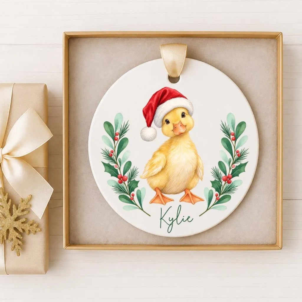 A ceramic ornament featuring a cute yellow duck wearing a Santa hat, surrounded by green leaves and red berries, with the name "Kylie" written on it.