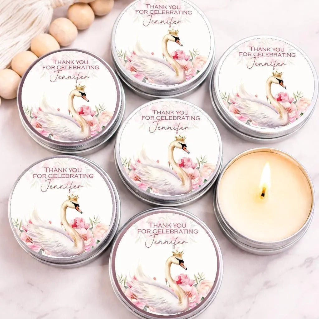 a collection of round tin candles with a swan design, arranged on a marble surface. The candles are labeled with the name "Jennifer" and are accompanied by a candle in the foreground.