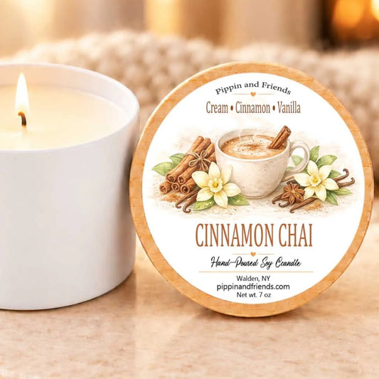 a white candle with a label that reads "Cinnamon Chai" and "Hand-Drawn Soy Candle" on a marble surface.