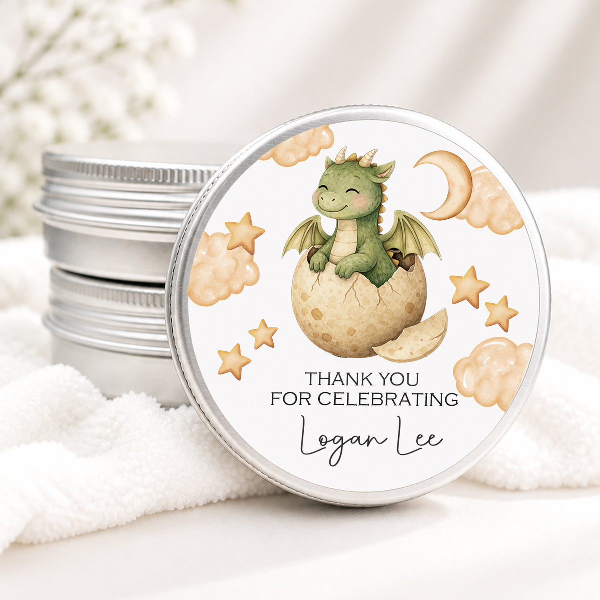 Personalized dragon baby shower candle favor in a silver tin featuring a watercolor baby dragon hatching from an egg surrounded by stars, clouds, and a crescent moon. Custom label reads “Thank You for Celebrating Logan Lee,” creating a magical keepsake for a dragon-themed baby shower.