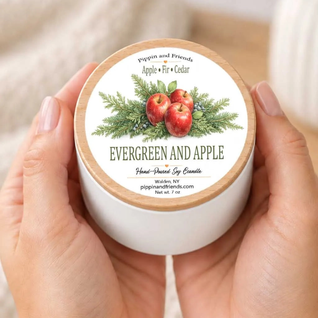 A person's hands holding a white container with a label featuring an illustration of apples and pine branches.