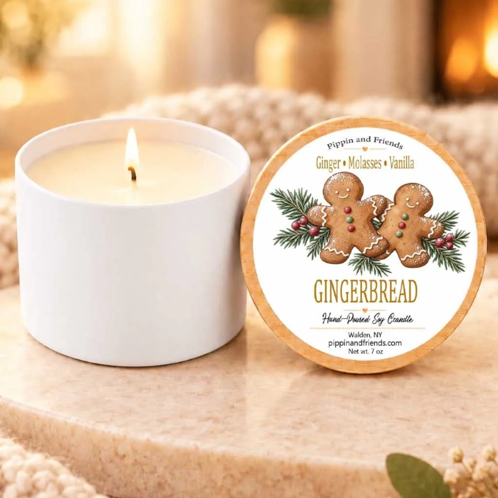 a white candle with a gingerbread and vanilla scent, placed on a wooden surface next to a round lid with a label.