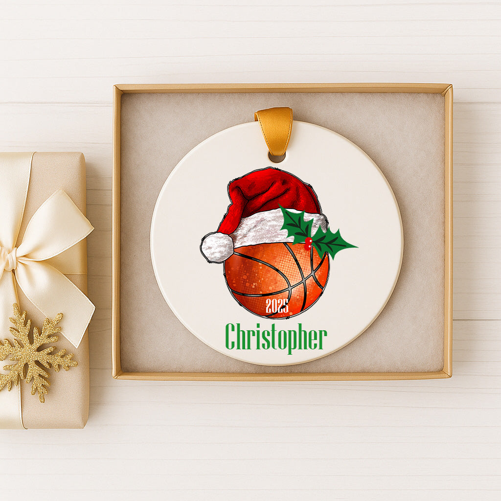 A basketball ornament with a Santa hat and holly leaves, and the name "Christopher" written on it, is displayed in a white box.