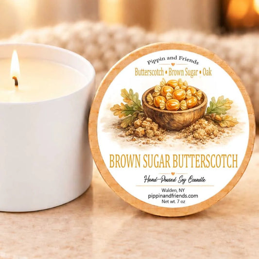 a brown sugar butterscotch candle and a white candle on a table, with a blurred background that includes a fireplace.