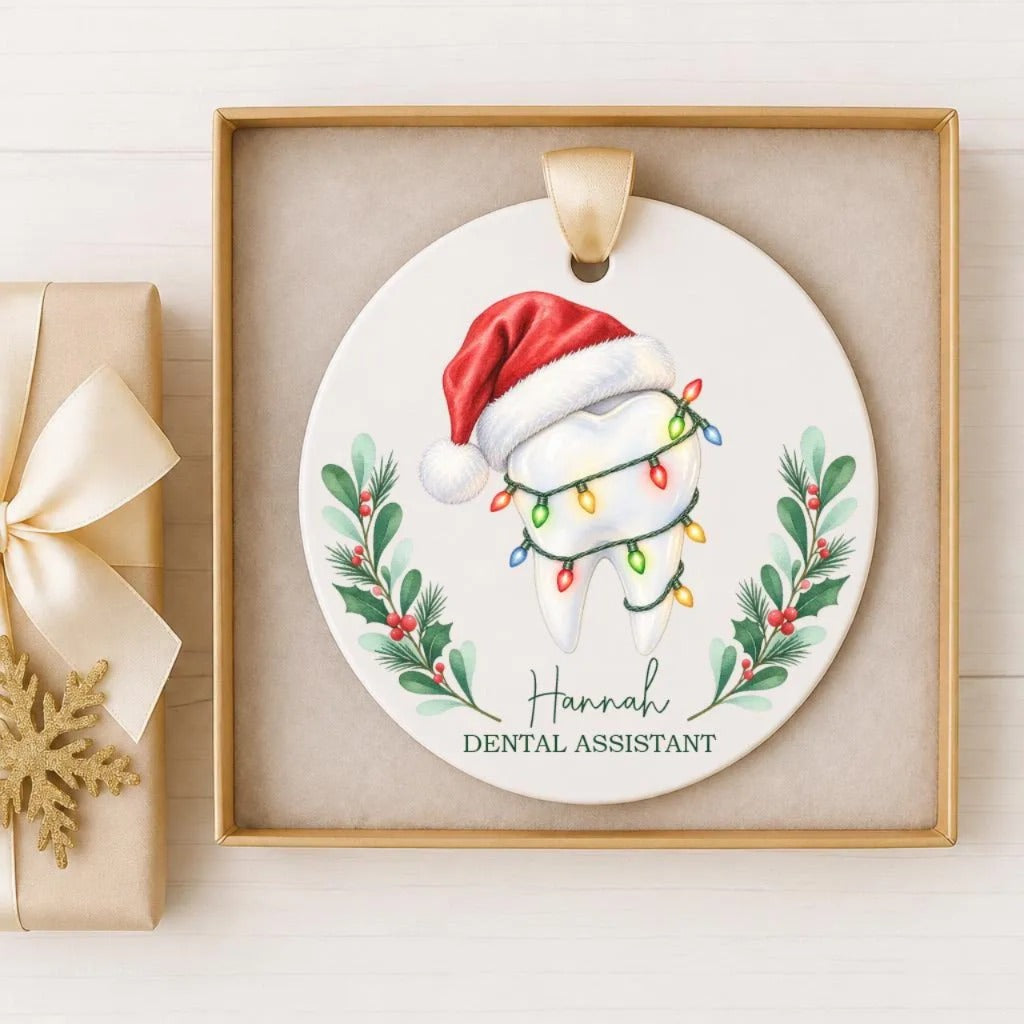 A ceramic ornament with a tooth and a Santa hat, surrounded by holiday decorations such as holly leaves and berries. The ornament is displayed in a wooden frame.