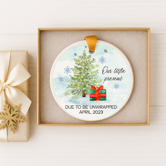 A decorative ornament with a Christmas tree and a gift box, placed on a white surface.