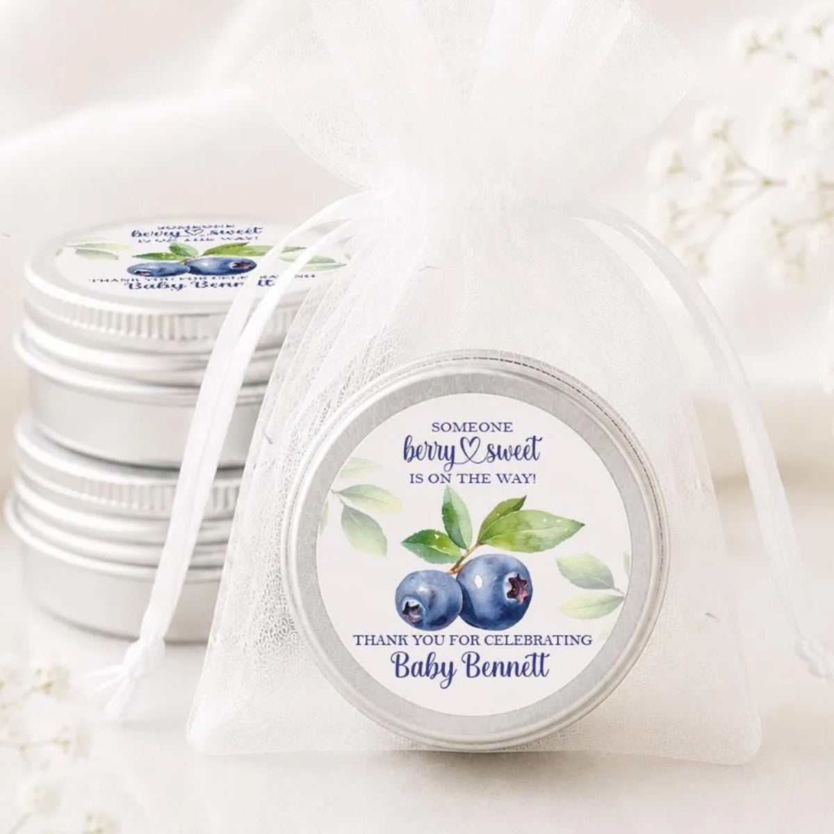 a set of silver tin jars with white labels, each containing a blueberry and leaf design. The labels are white and have text on them, including a message about someone being sweet and a thank you for celebrating Baby Bennett.