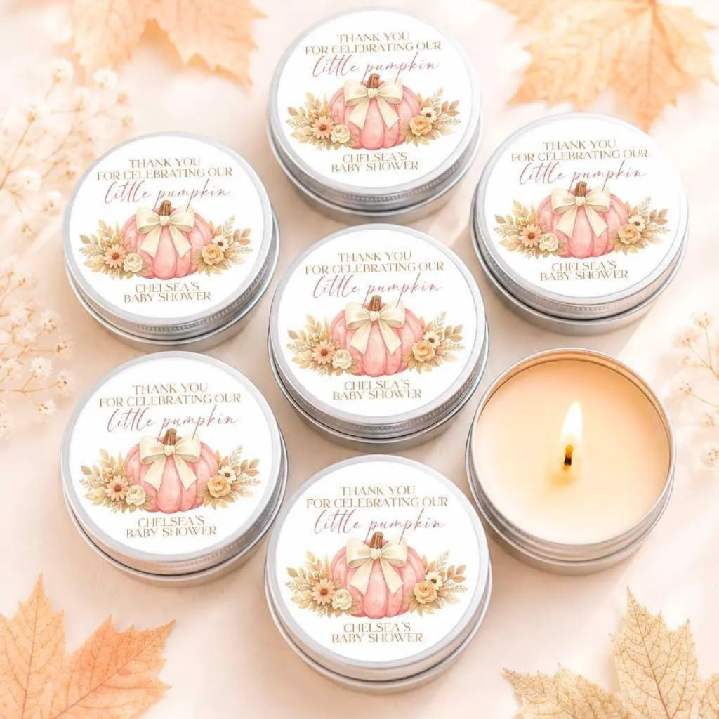 six silver tins with white labels, each featuring a pink pumpkin and text that reads "Thank you for celebrating our little pumpkin" and "CHELSEA'S BABY SHOWER". The tins are arranged in a circular pattern, with one candle in the center.