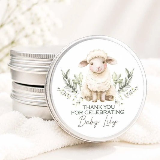 A round tin lid with a white sheep illustration and the text "Thank you for celebrating Baby Lilly" on it.