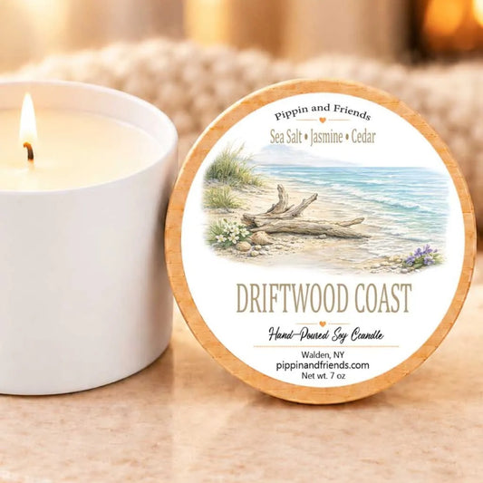 a white candle next to a round label with a beach scene and text, and a blurred background that appears to be a beige fabric or blanket.