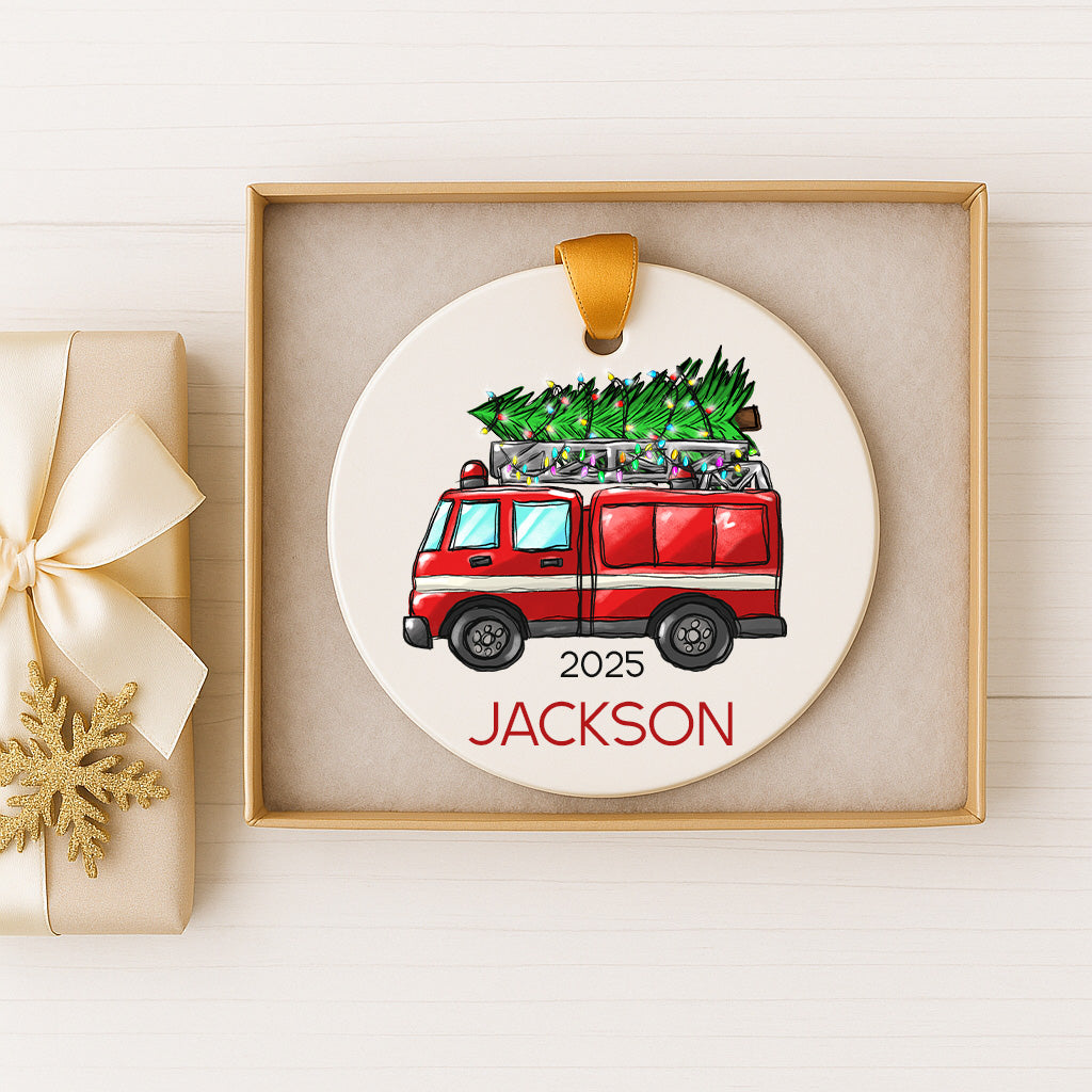 A Christmas ornament featuring a red fire truck carrying a Christmas tree, with the name "JACKSON" written below it.