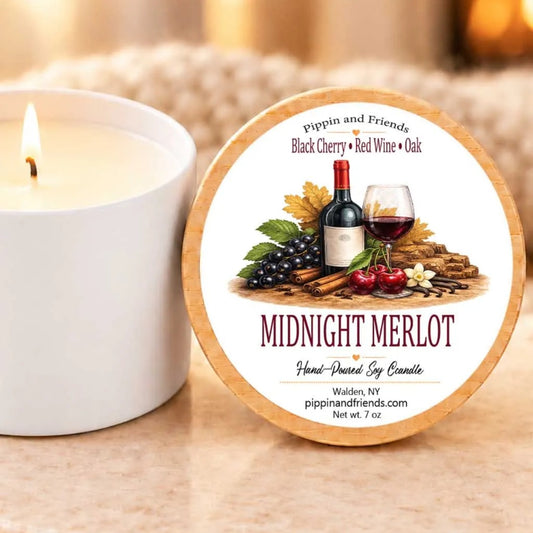 a white candle with a label that reads "Midnight Merlot" and "Hand-Poured Soy Candle" on a wooden holder.