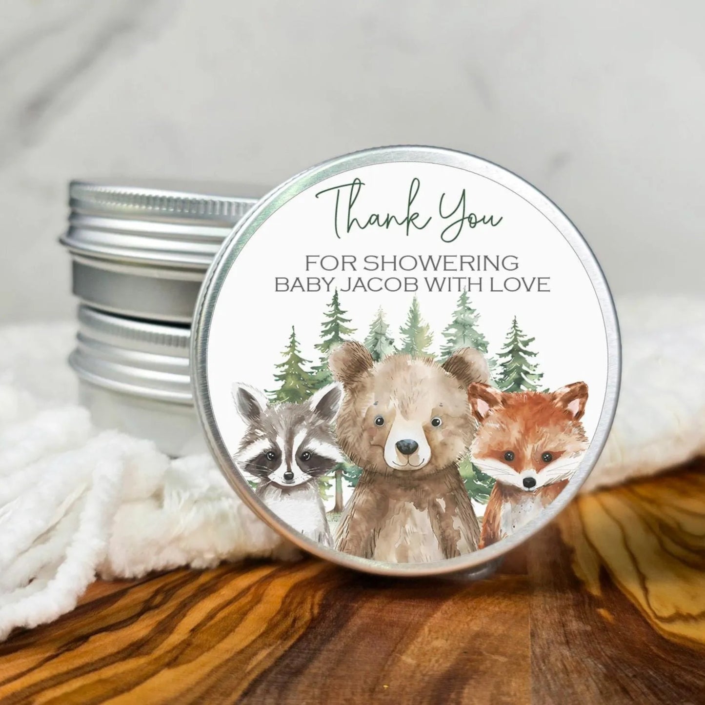 A round tin lid with a label featuring a bear, raccoon, and fox, along with the text "Thank You for showering Baby Jacob with love".