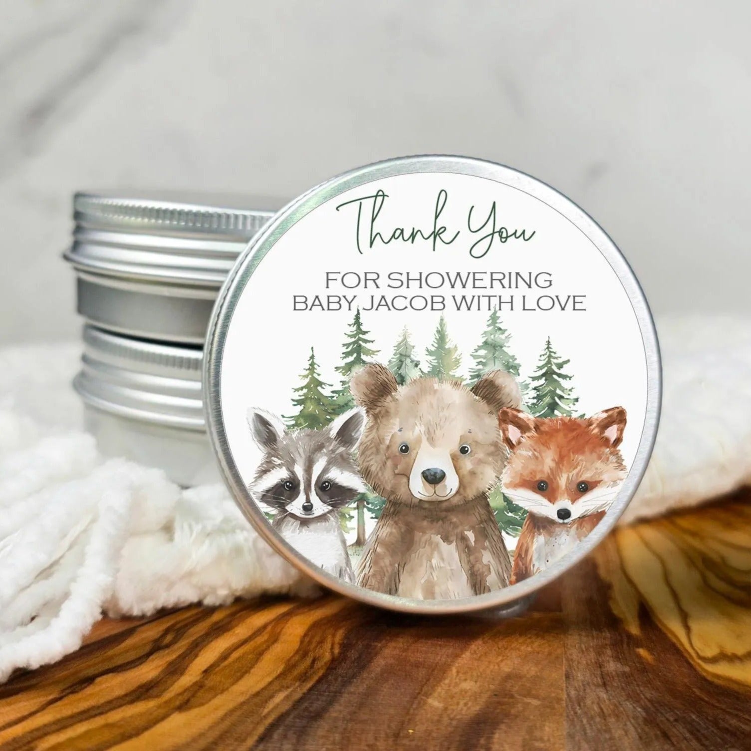 A round tin lid with a label featuring a bear, raccoon, and fox, along with the text "Thank You for showering Baby Jacob with love".