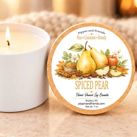 a white candle with a label that reads "Spiced Pear Hand-Dried Soy Candle" and " Walden, NY pippinandfriends.com net wt 7 oz". The candle is placed next to a white candle holder, creating a cozy and inviting scene.